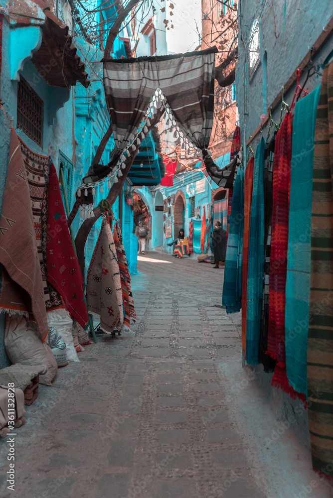 Chefchaouen, Morocco - APRIL 18 2019 View of a narrow street with steps and products for sale in the blue city on a sunny spring day
