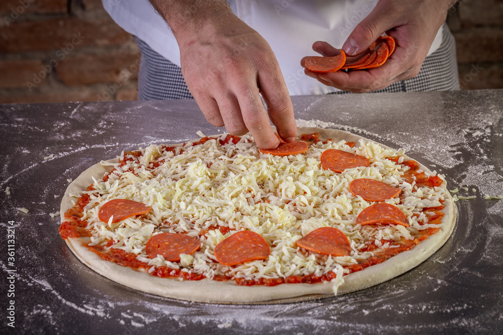 Fresh pizza dough being prepared with tomato sauce, mozzarella and pepperoni. The process of making pizza
