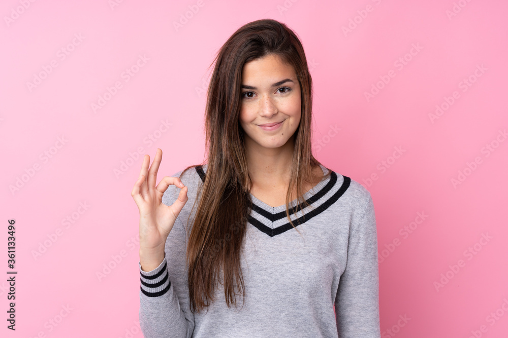 Teenager girl over isolated pink background showing an ok sign with fingers Teenager girl over isolated pink background showing an ok sign with fingers