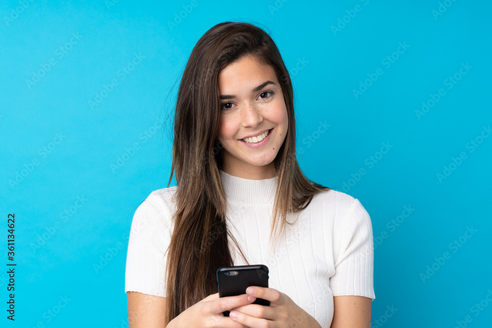 Teenager girl over isolated blue background sending a message with the mobile Teenager girl over isolated blue background sending a message with the mobile