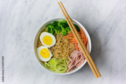 Ramen noodles soup in white bowl with eggs, scallion, chives, broccoli, carrot, top off view, copy space
