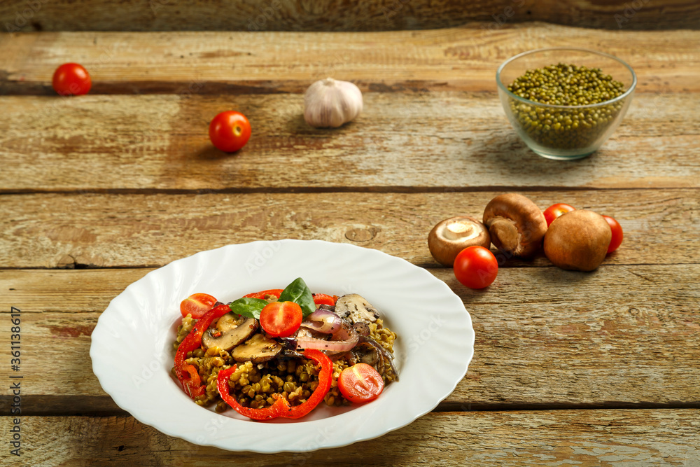 On a wooden table is a white plate of boiled mung bean with mushrooms and vegetables next to the ingredients. On a wooden table is a white plate of boiled mung bean with mushrooms and vegetables next to the ingredients.