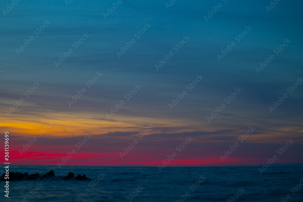 colorful yellow pink sunset on rocky beach with cloudy sky