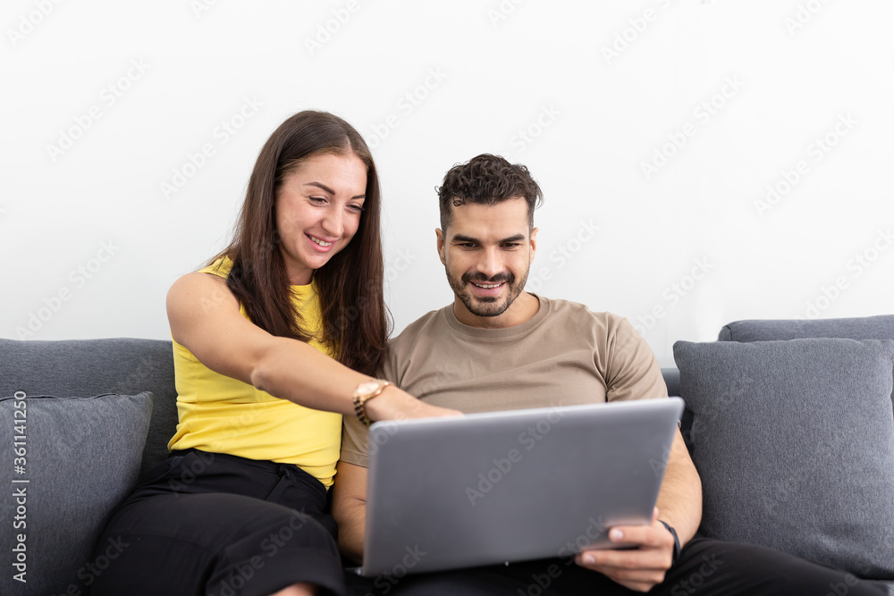 Happy young couple spending time together at home. Couple caucasian using notebook computer together on sofa in the living room at home for shopping online, browsing internet or meeting working video Happy young couple spending time together at home. Couple caucasian using notebook computer together on sofa in the living room at home for shopping online, browsing internet or meeting working video