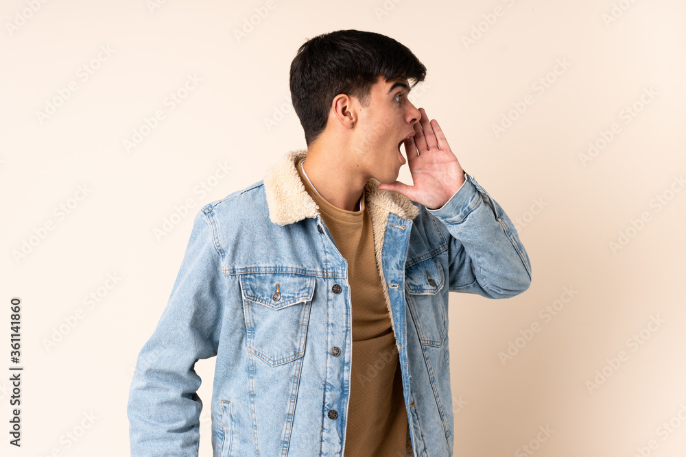 Handsome man over isolated beige background shouting with mouth wide open to the side Handsome man over isolated beige background shouting with mouth wide open to the side