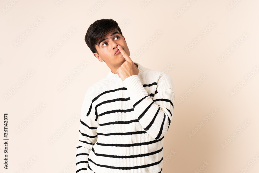 Handsome man over isolated beige background having doubts while looking up Handsome man over isolated beige background having doubts while looking up