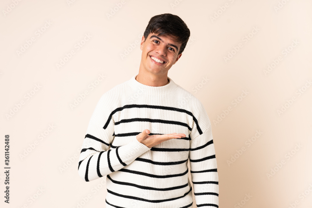 Obraz premium Handsome man over isolated beige background presenting an idea while looking smiling towards