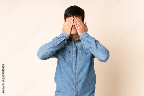 Handsome man over isolated beige background covering eyes by hands