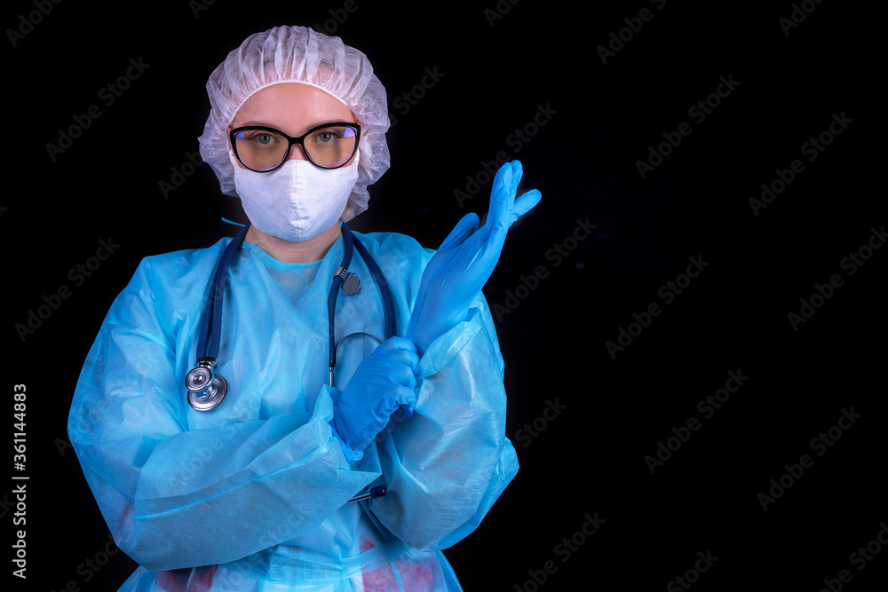 A doctor on a black background puts on medical gloves. A doctor in a protective mask and clothing for the treatment of coronavirus A doctor on a black background puts on medical gloves. A doctor in a protective mask and clothing for the treatment of coronavirus