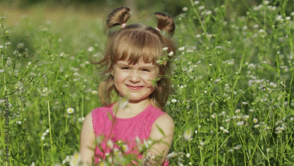 Little blonde child girl in pink dress stay on flower chamomile grass meadow. Bouquet of daisies