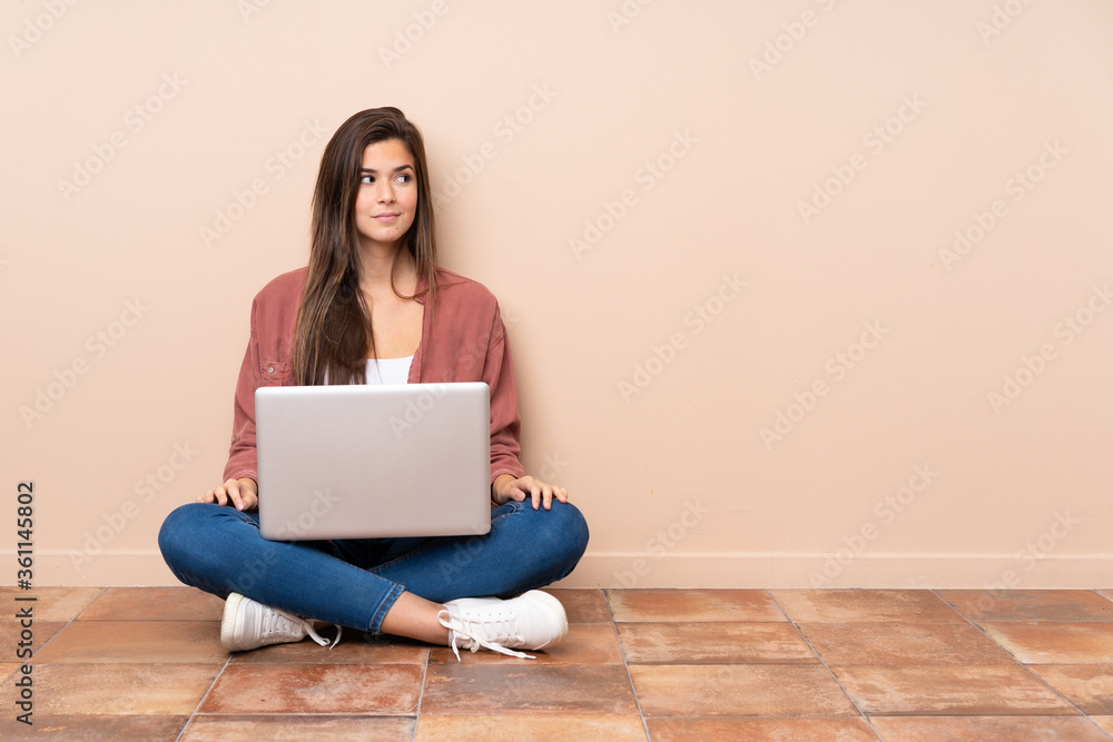 Naklejka premium Teenager student girl sitting on the floor with a laptop making doubts gesture looking side