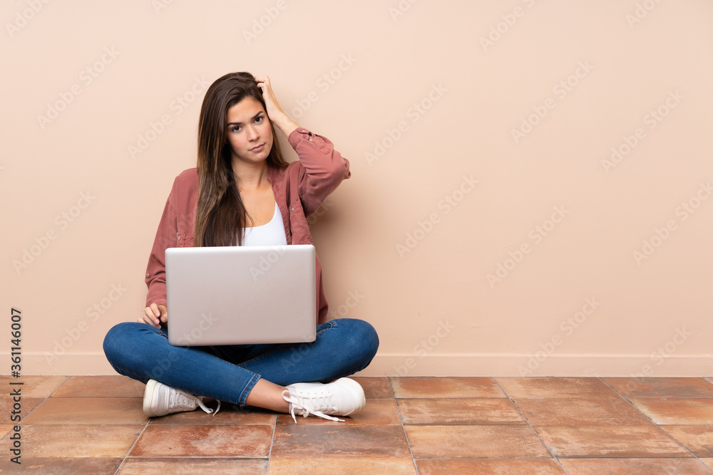 Teenager student girl sitting on the floor with a laptop with an expression of frustration and not understanding Teenager student girl sitting on the floor with a laptop with an expression of frustration and not understanding