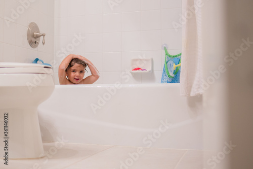 Boy playing in bath with toys washing his hair 