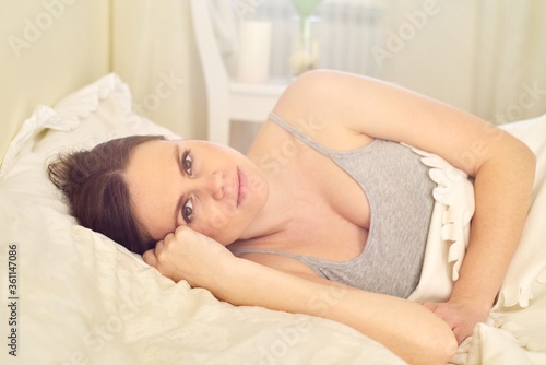 Smiling young woman lying in bed looking at the camera