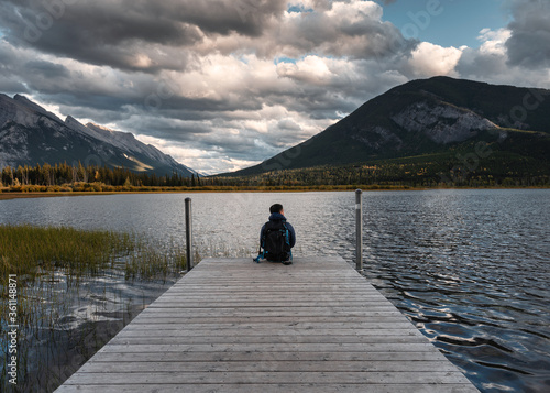 Vászonkép Man backpacker sitting on wooden pier in Vermillion lake at Banff national park