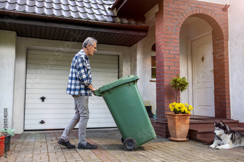 Senior man rolling garbage can
