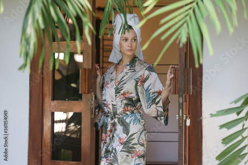 Young woman in silk robe and hair wrapped in a towel enjoy a vacation day in a wooden summer cottage. Wellbeing lifestyle concept. Idyllic remote tropical summer vacation. photo