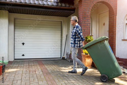 Senior man rolling garbage can
