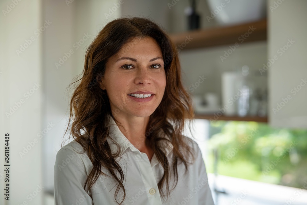Authentic close up shot of an attractive brunette happy woman is smiling in camera in a kitchen at home. Authentic close up shot of an attractive brunette happy woman is smiling in camera in a kitchen at home.