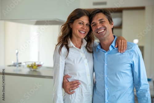 Authentic shot of lovely happy smiling married  embraced couple is smiling in camera in a kitchen at home.