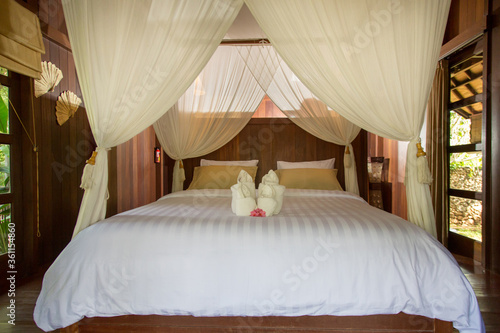 King size bed with mosquito net, bedroom interior in calm white colors, no people © triocean