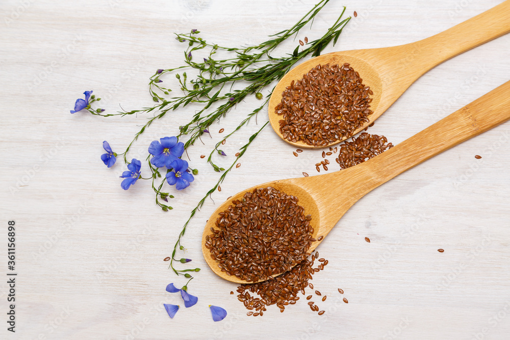 Flax seeds and a blue flower of flax on a wooden background. Healthy food and drink concept. Flax seeds is a superfood Flax seeds and a blue flower of flax on a wooden background. Healthy food and drink concept. Flax seeds is a superfood