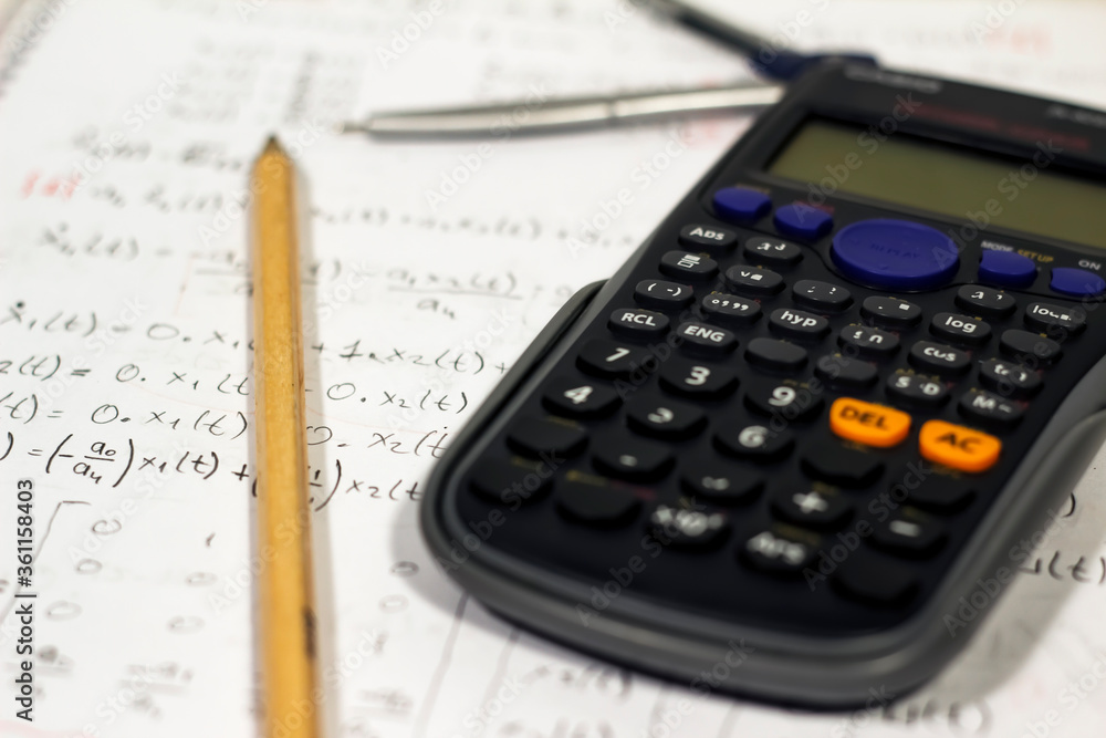 Equations and math writings on notebook with calculator, pencil and compasses Equations and math writings on notebook with calculator, pencil and compasses