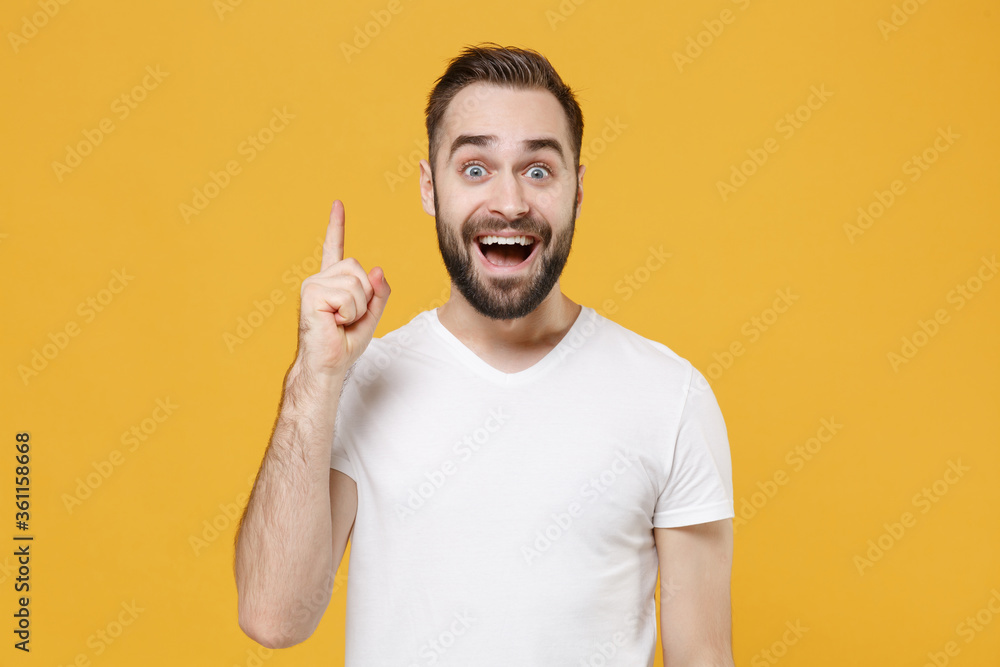 Excited young bearded man guy in white casual t-shirt posing isolated on yellow background studio portrait. People lifestyle concept. Mock up copy space. Holding index finger up with great new idea. Excited young bearded man guy in white casual t-shirt posing isolated on yellow background studio portrait. People lifestyle concept. Mock up copy space. Holding index finger up with great new idea.