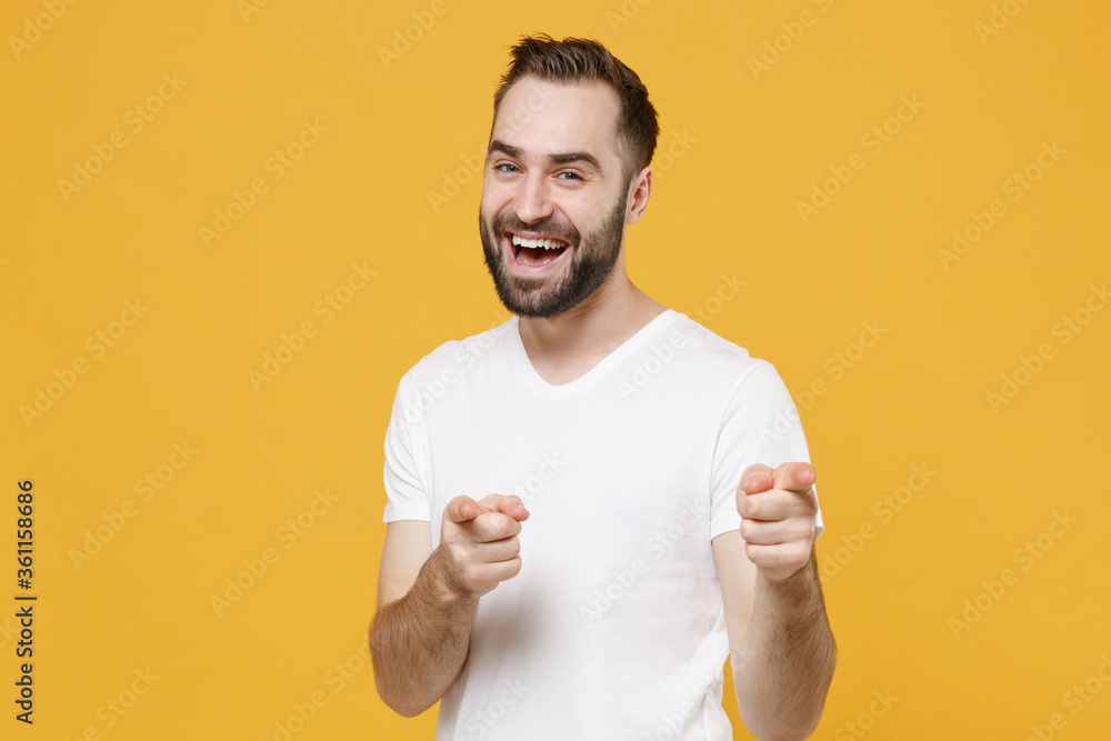 Cheerful young bearded man guy 20s in white casual t-shirt posing isolated on yellow wall background studio portrait. People lifestyle concept. Mock up copy space. Pointing index fingers on camera. Cheerful young bearded man guy 20s in white casual t-shirt posing isolated on yellow wall background studio portrait. People lifestyle concept. Mock up copy space. Pointing index fingers on camera.