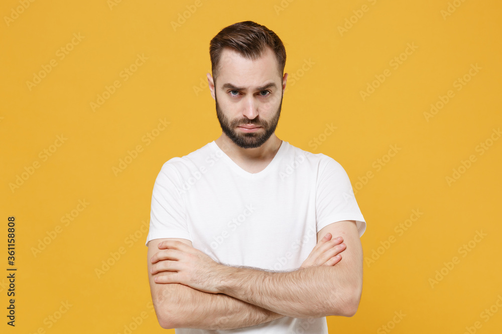 Displeased offended young bearded man guy in white casual t-shirt posing isolated on yellow background studio portrait. People emotions lifestyle concept. Mock up copy space. Holding hands crossed. Displeased offended young bearded man guy in white casual t-shirt posing isolated on yellow background studio portrait. People emotions lifestyle concept. Mock up copy space. Holding hands crossed.