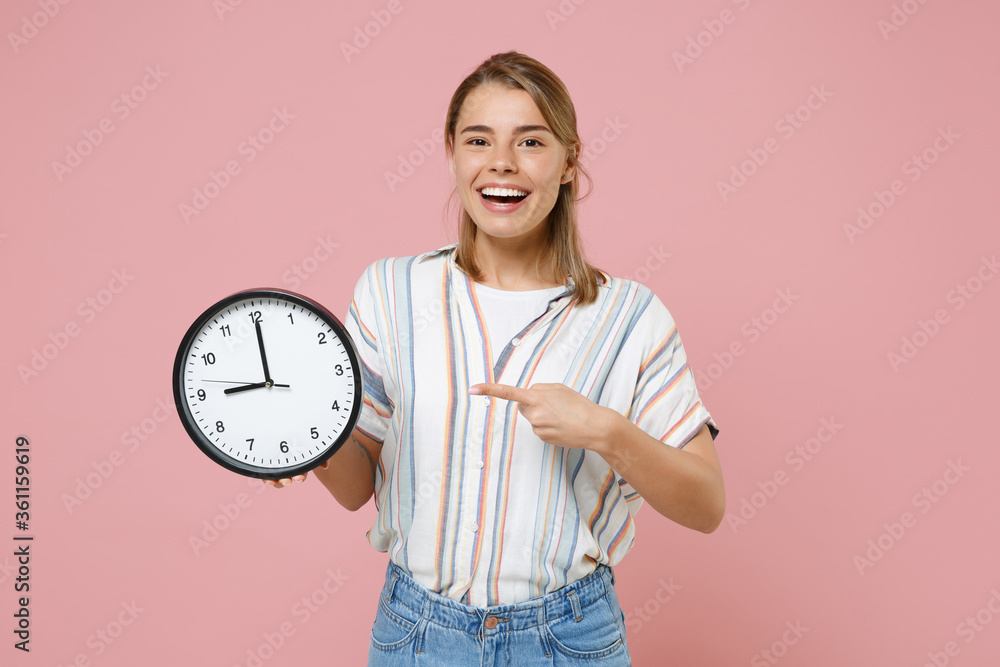 Funny young blonde woman girl in casual striped shirt posing isolated on pastel pink background studio portrait. People emotions lifestyle concept. Mock up copy space. Pointing index finger on clock. Funny young blonde woman girl in casual striped shirt posing isolated on pastel pink background studio portrait. People emotions lifestyle concept. Mock up copy space. Pointing index finger on clock.