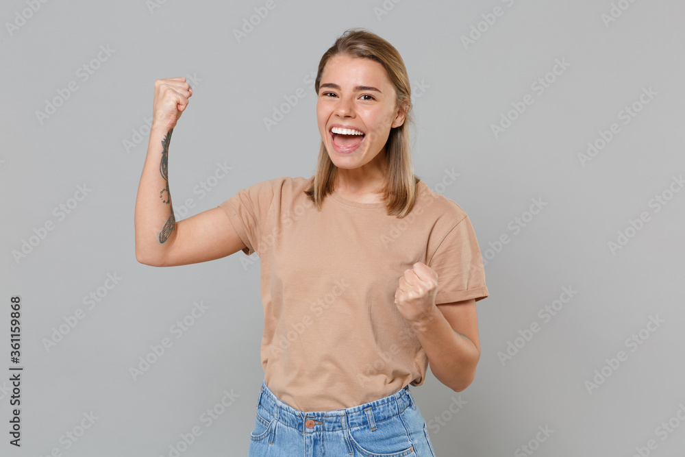 Joyful young blonde woman girl in casual beige t-shirt posing isolated on gray background studio portrait. People sincere emotions lifestyle concept. Mock up copy space. Clenching fists like winner. Joyful young blonde woman girl in casual beige t-shirt posing isolated on gray background studio portrait. People sincere emotions lifestyle concept. Mock up copy space. Clenching fists like winner.
