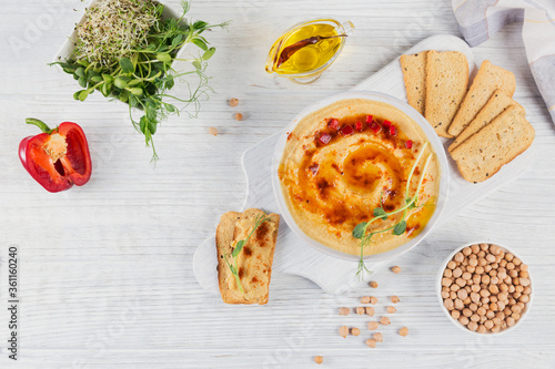 A bowl of chickpeas homemade hummus with olive oil, crispbread, microgreen and smoked paprika on white wooden background