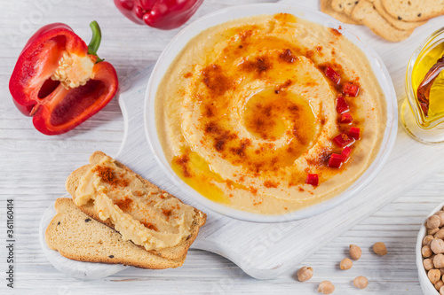 A bowl of chickpeas homemade hummus with olive oil, crispbread and smoked paprika on white wooden background