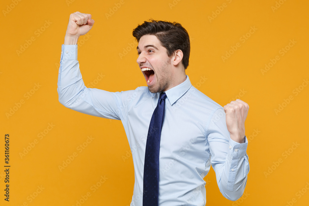 Screaming young business man in classic blue shirt tie posing isolated on yellow wall background studio portrait. Achievement career wealth business concept. Mock up copy space. Doing winner gesture. Screaming young business man in classic blue shirt tie posing isolated on yellow wall background studio portrait. Achievement career wealth business concept. Mock up copy space. Doing winner gesture.