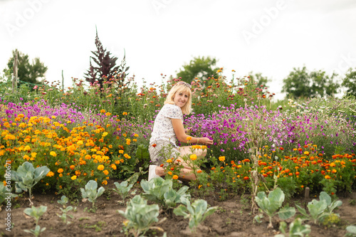 Tablou canvas Happy girl sitting on a flower bed near the cabbage in the garden in a country house and posing for the camera with a smile on his face