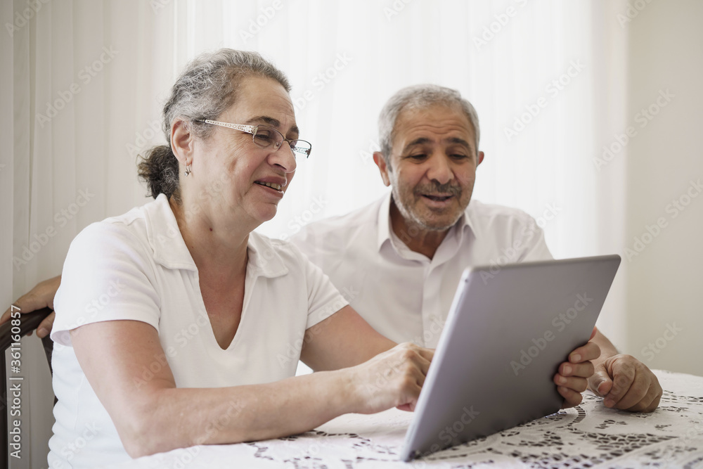 Happy senior couple wave having video call on laptop talking with relatives, smiling aged husband and wife sit on couch at home communicating via online using computer. Elderly and technology concept