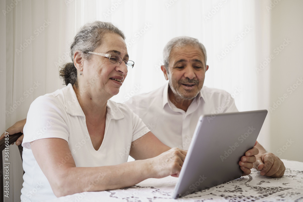 Happy senior couple wave having video call on laptop talking with relatives, smiling aged husband and wife sit on couch at home communicating via online using computer. Elderly and technology concept Happy senior couple wave having video call on laptop talking with relatives, smiling aged husband and wife sit on couch at home communicating via online using computer. Elderly and technology concept