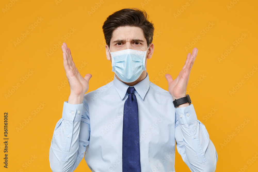 Perplexed young business man in classic blue shirt tie sterile face mask isolated on yellow background studio. Epidemic pandemic coronavirus 2019-ncov sars covid-19 flu virus concept. Spreading hands. Perplexed young business man in classic blue shirt tie sterile face mask isolated on yellow background studio. Epidemic pandemic coronavirus 2019-ncov sars covid-19 flu virus concept. Spreading hands.