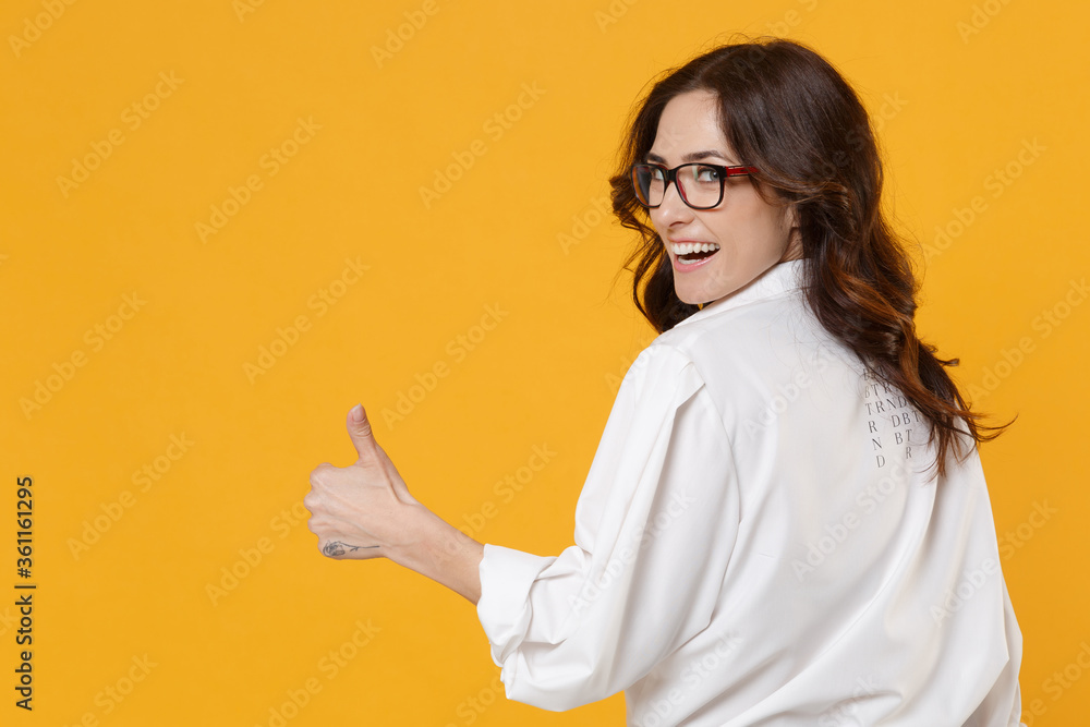 Back rear view of funny young business woman in white shirt glasses isolated on yellow background. Achievement career wealth business concept. Mock up copy space. Showing thumb up, looking camera. Back rear view of funny young business woman in white shirt glasses isolated on yellow background. Achievement career wealth business concept. Mock up copy space. Showing thumb up, looking camera.