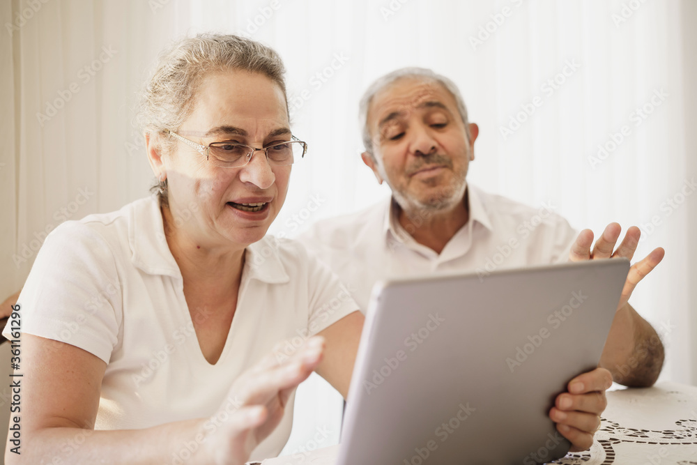 The elderly couple trying to use the tablet show each other something on the screen. old couple is trying to talk to their grandchildren. old couple is trying to talk to their children.