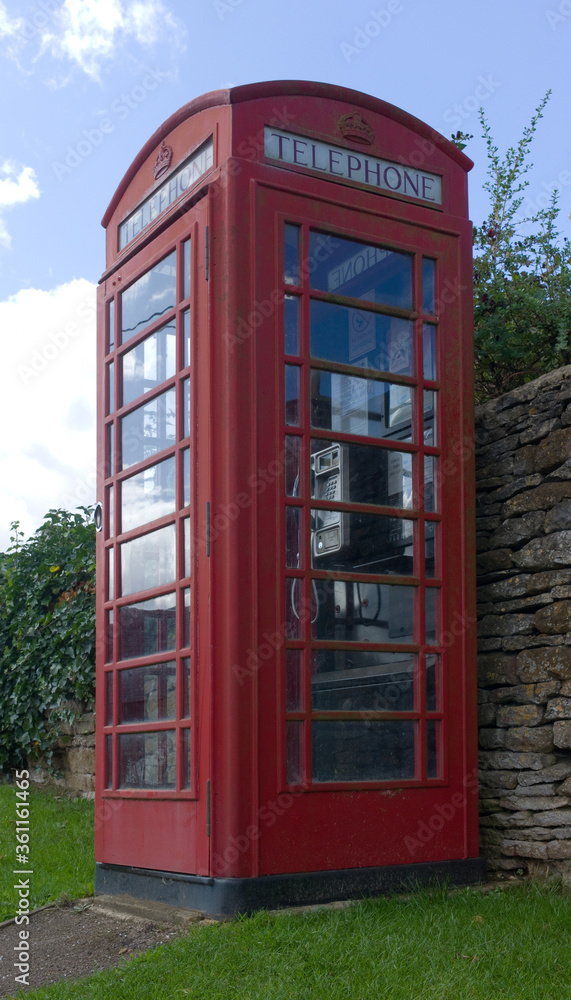 A traditional red telephone box in grass against a stone wall A traditional red telephone box in grass against a stone wall