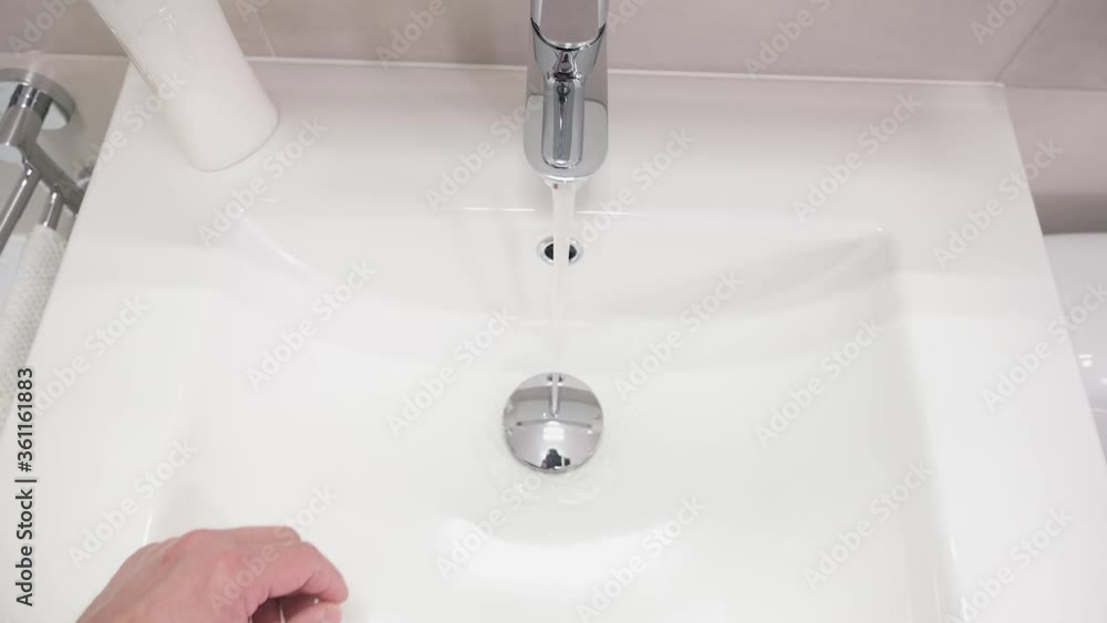 Male hand turning water tap for pouring water into sink in bathroom. Flowing water. Adult man turning off tap. Top view. Male hand turning water tap for pouring water into sink in bathroom. Flowing water. Adult man turning off tap. Top view.