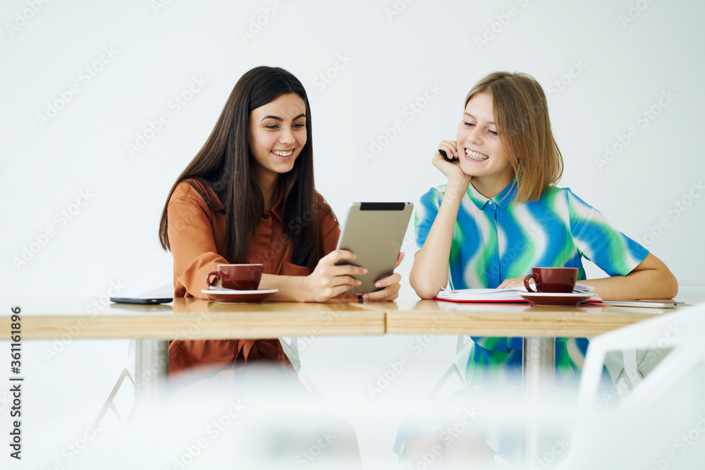 Cheerful young attractive friends enjoying free time together in coffee shop watching funny videos from social networks via digital tablet connected to wifi sitting against copy space for advertising Cheerful young attractive friends enjoying free time together in coffee shop watching funny videos from social networks via digital tablet connected to wifi sitting against copy space for advertising