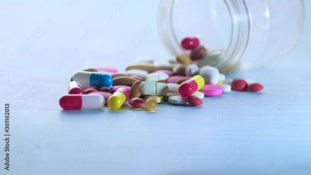 colorful pills spilling from a container on table colorful pills spilling from a container on table