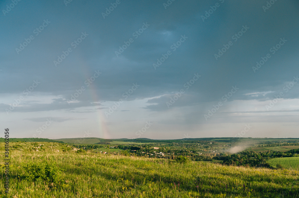 Beautiful landscape with untouched field, storm cloud and rainbow. Mountain landscape with a blue cloud and the beginning of a rainbow at sunset.