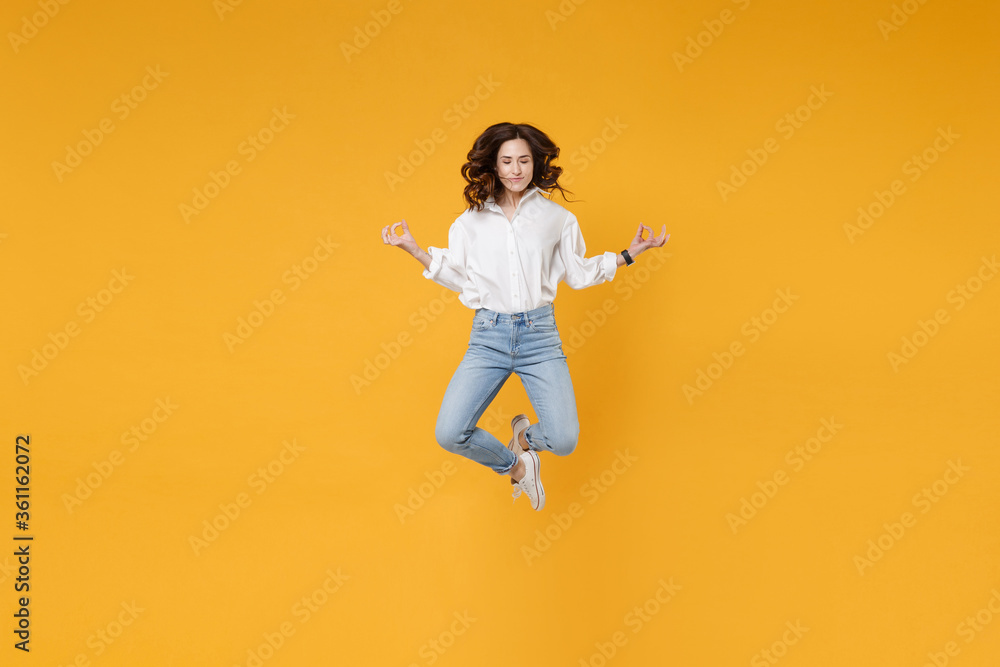 Young business woman in white shirt posing isolated on yellow background studio. Achievement career wealth business concept. Mock up copy space. Jump, hold hands in yoga gesture, relaxing meditating.