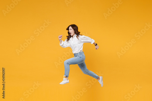 Side view of shocked young brunette business woman in white shirt posing isolated on yellow background in studio. Achievement career wealth business concept. Mock up copy space. Jumping like running. © ViDi Studio
