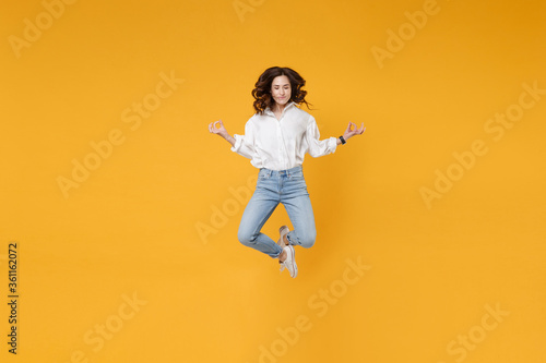 Young business woman in white shirt posing isolated on yellow background studio. Achievement career wealth business concept. Mock up copy space. Jump, hold hands in yoga gesture, relaxing meditating. © ViDi Studio