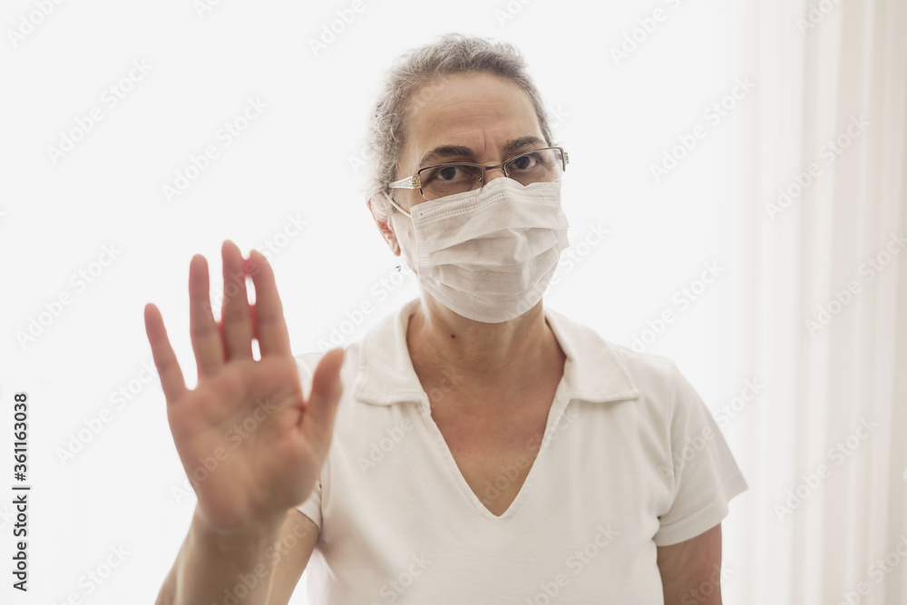 Isolated shot of old woman wearing mask showing stop sign with his open palm, saying that you better stay away from her. keeping hands in stop gesture, saying Stay away from me. Isolated shot of old woman wearing mask showing stop sign with his open palm, saying that you better stay away from her. keeping hands in stop gesture, saying Stay away from me.